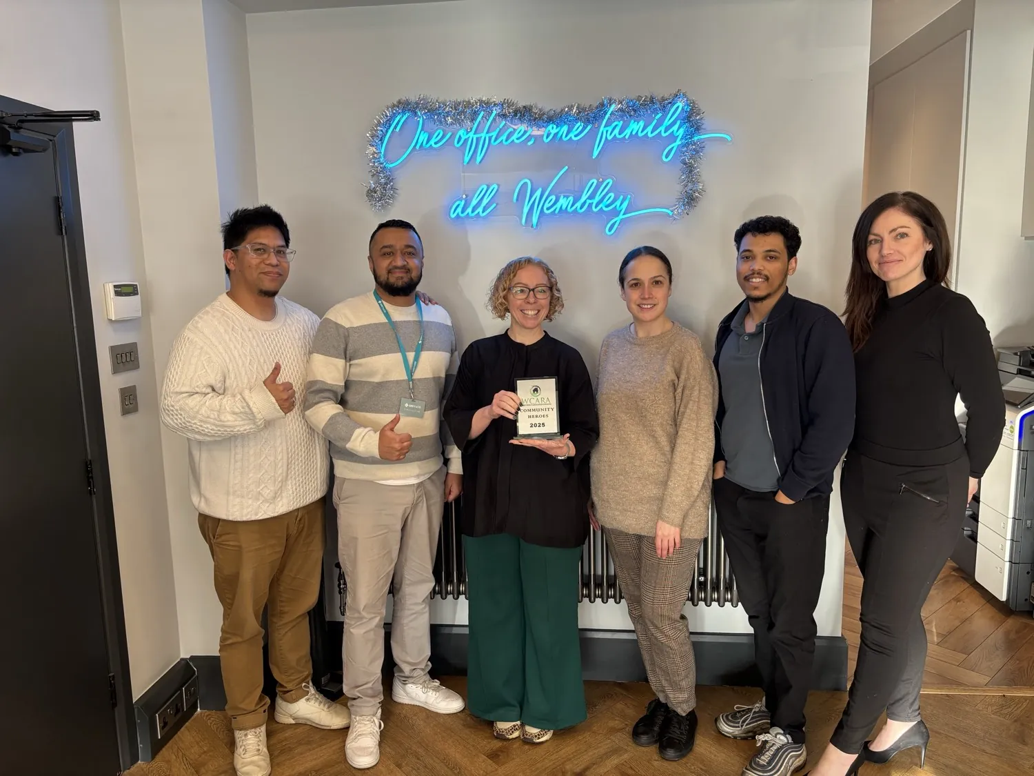A member agency team holding an award under a neon sign