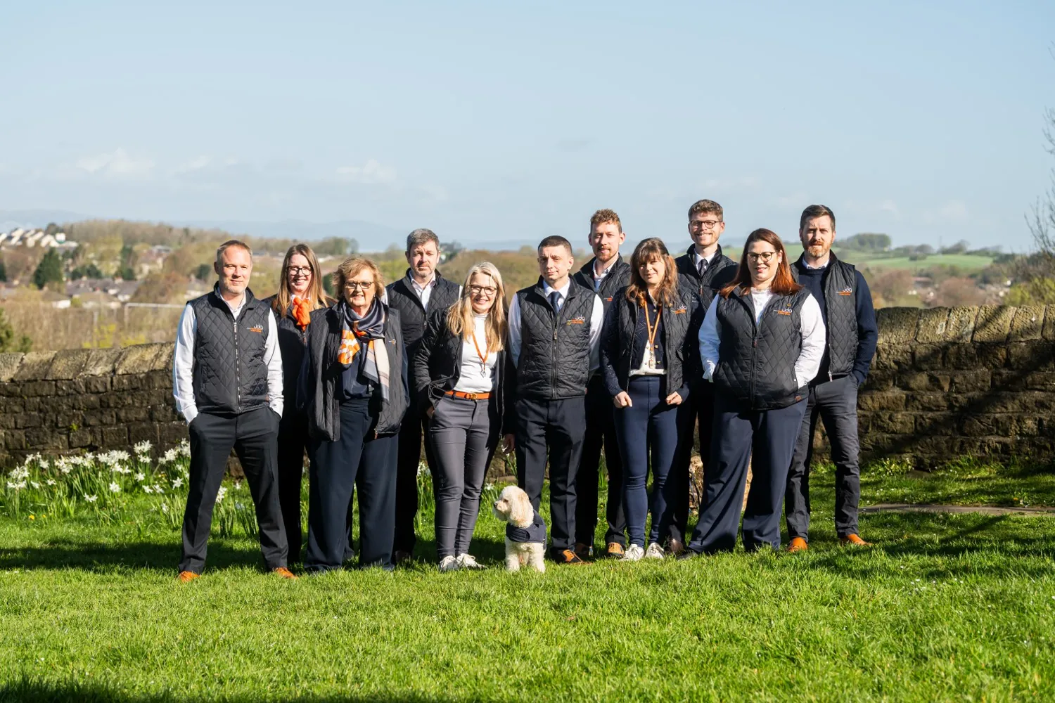 A member agency team lined up on grass with open countryside behind
