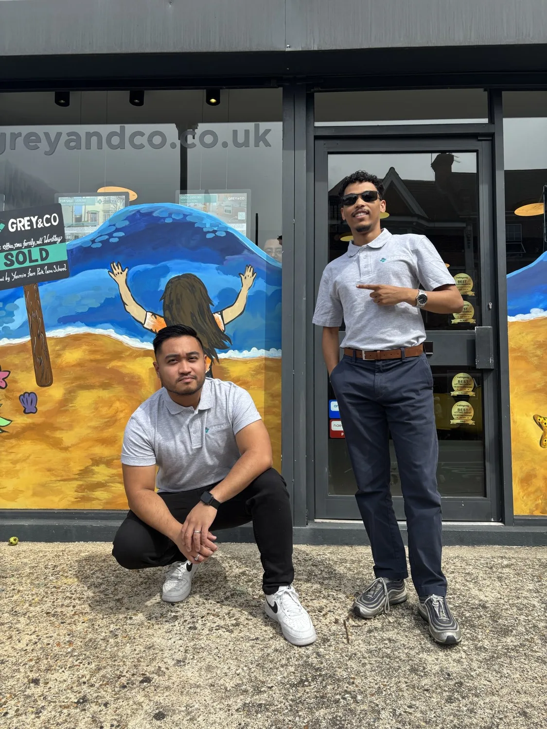 Two people from a member agency in front of a painted seaside mural on their shopfront